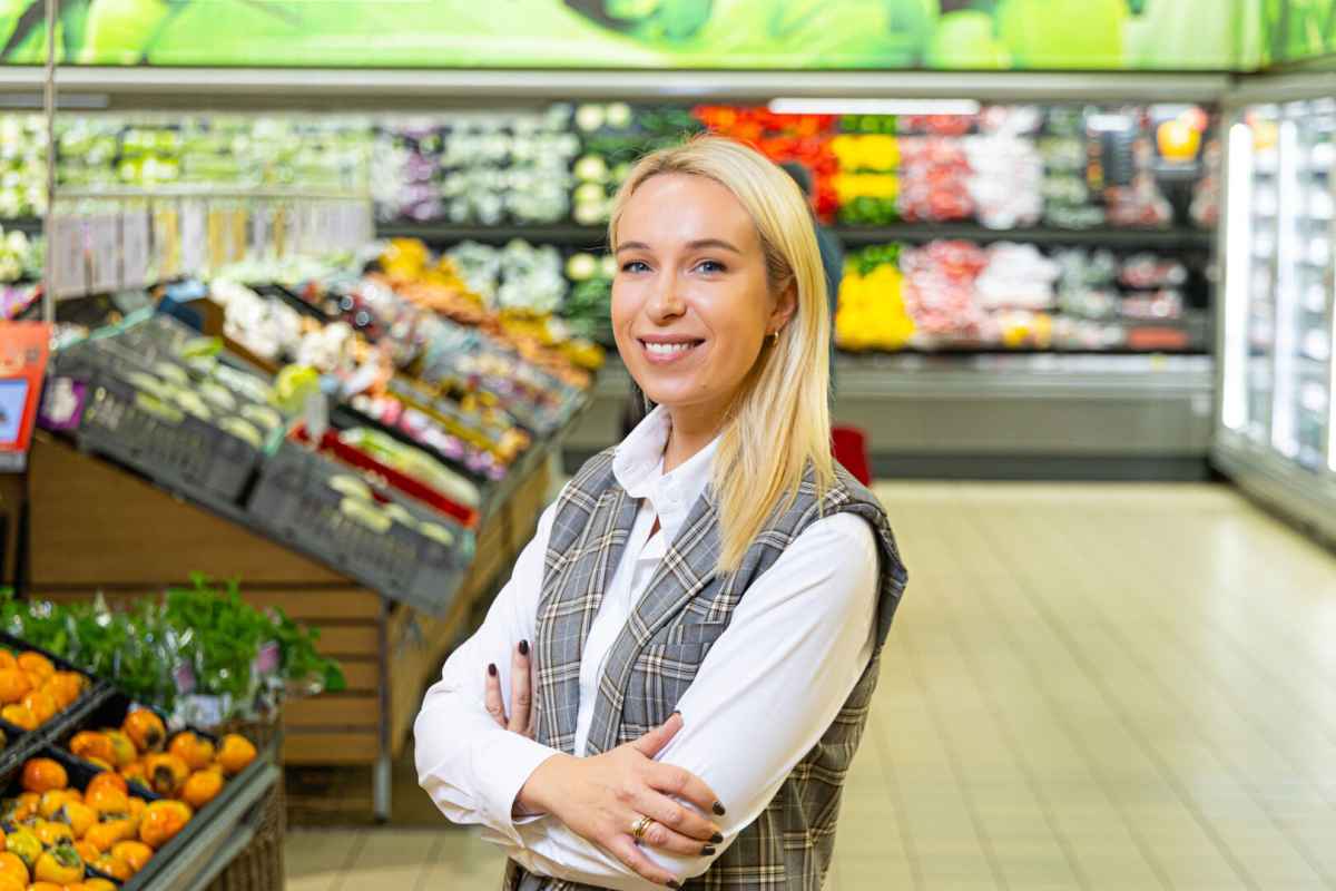 Moteris su susikryžiavusiomis rankomis stovi maisto prekių skyriuje.