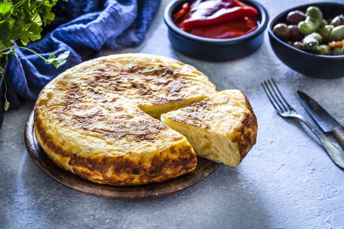 Keptas bulvių tortas ant medinio padėklo su atpjauta riekle ir padažu.